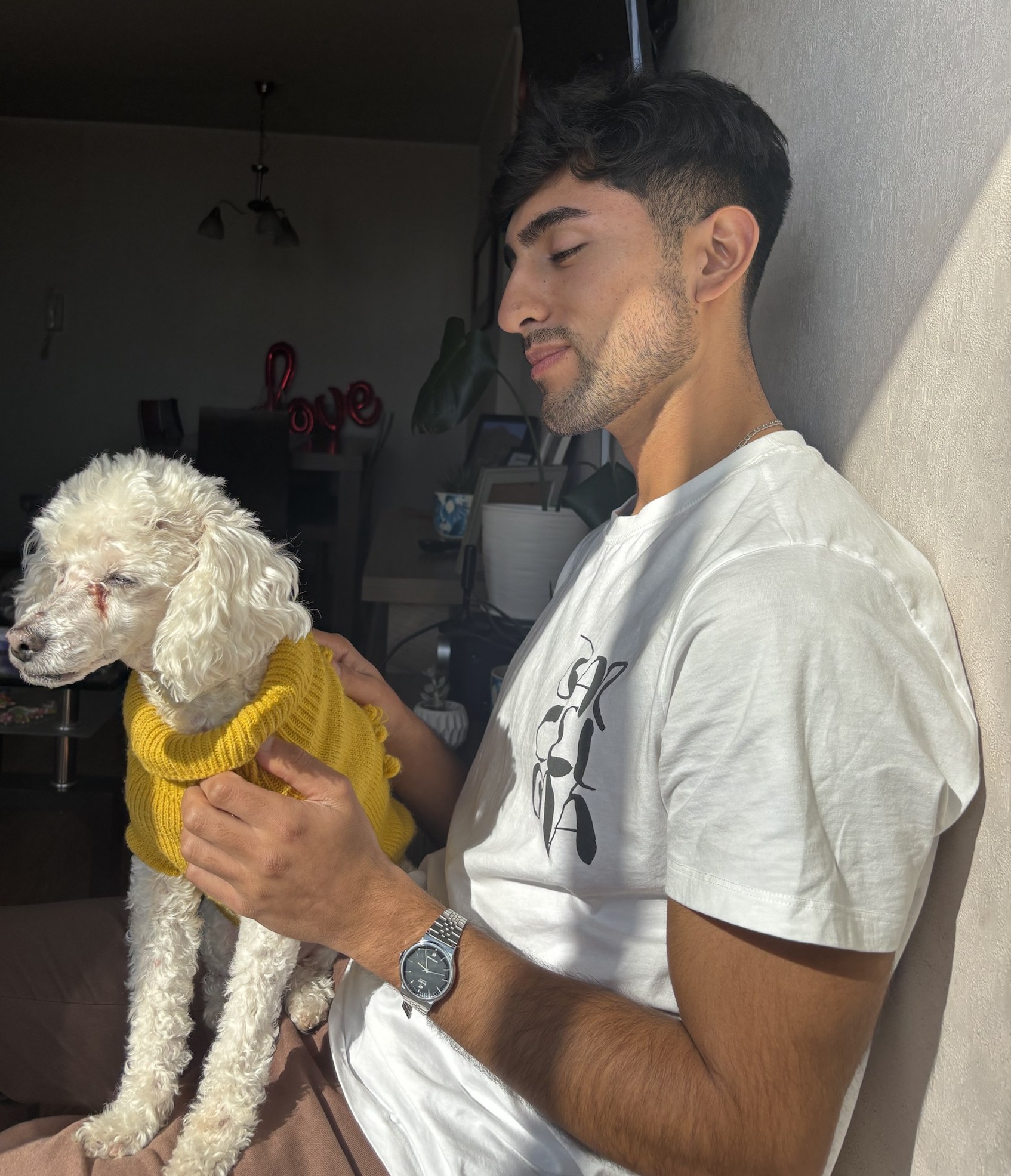 Francisco Farías en su casa, con luz de tarde, sosteniendo a su perro con un chaleco amarillo